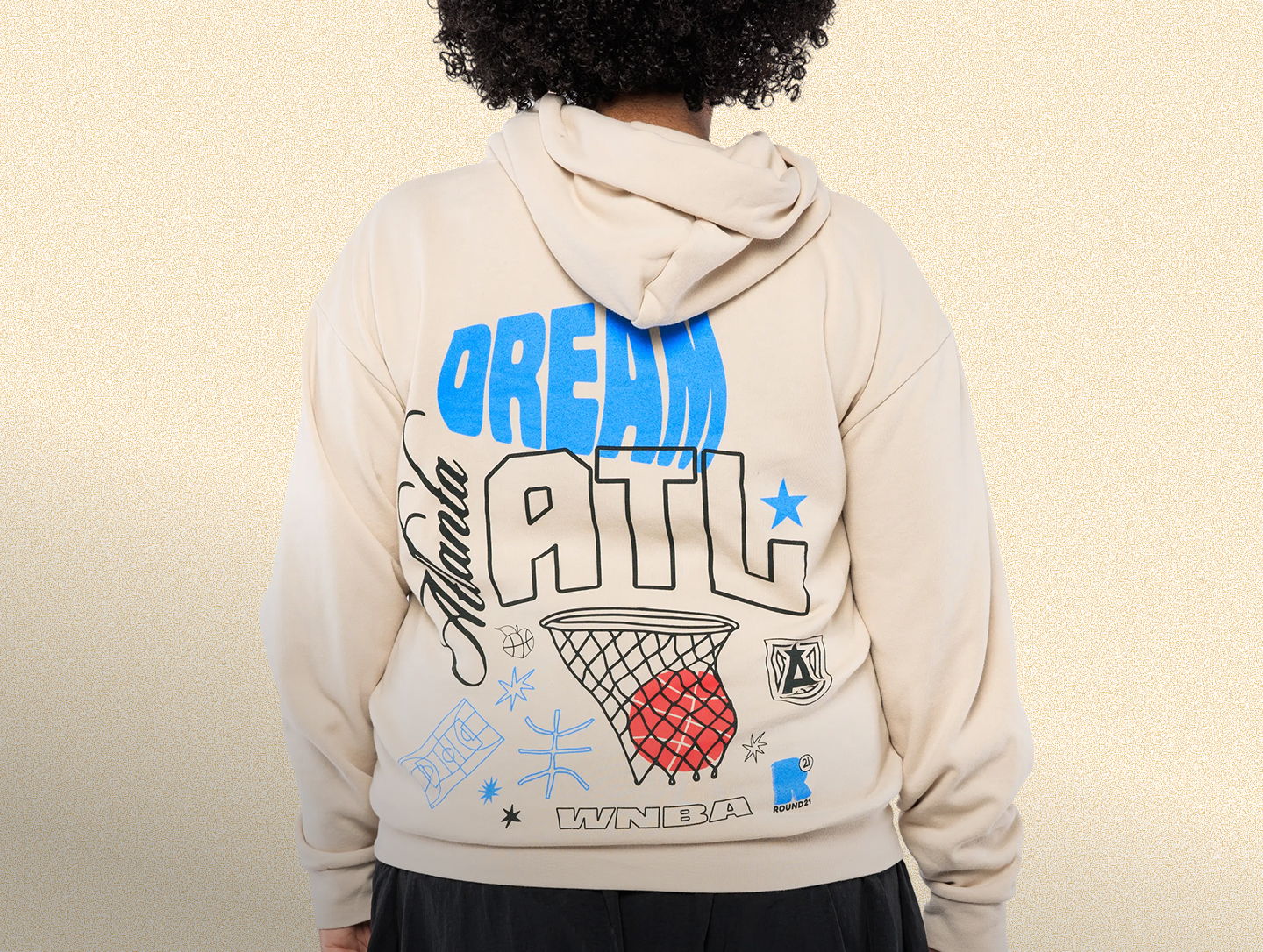 Person wearing a hoodie with 'Dream ATL' text and graphics on the back against a beige background