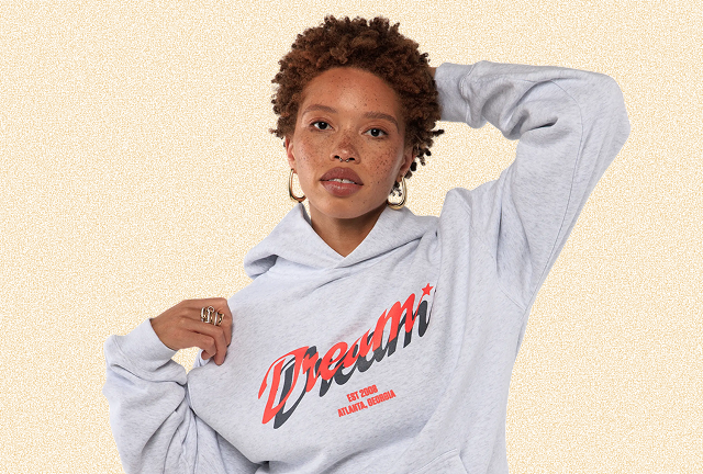 Woman wearing a gray hoodie with 'Dream' printed on it against a beige background