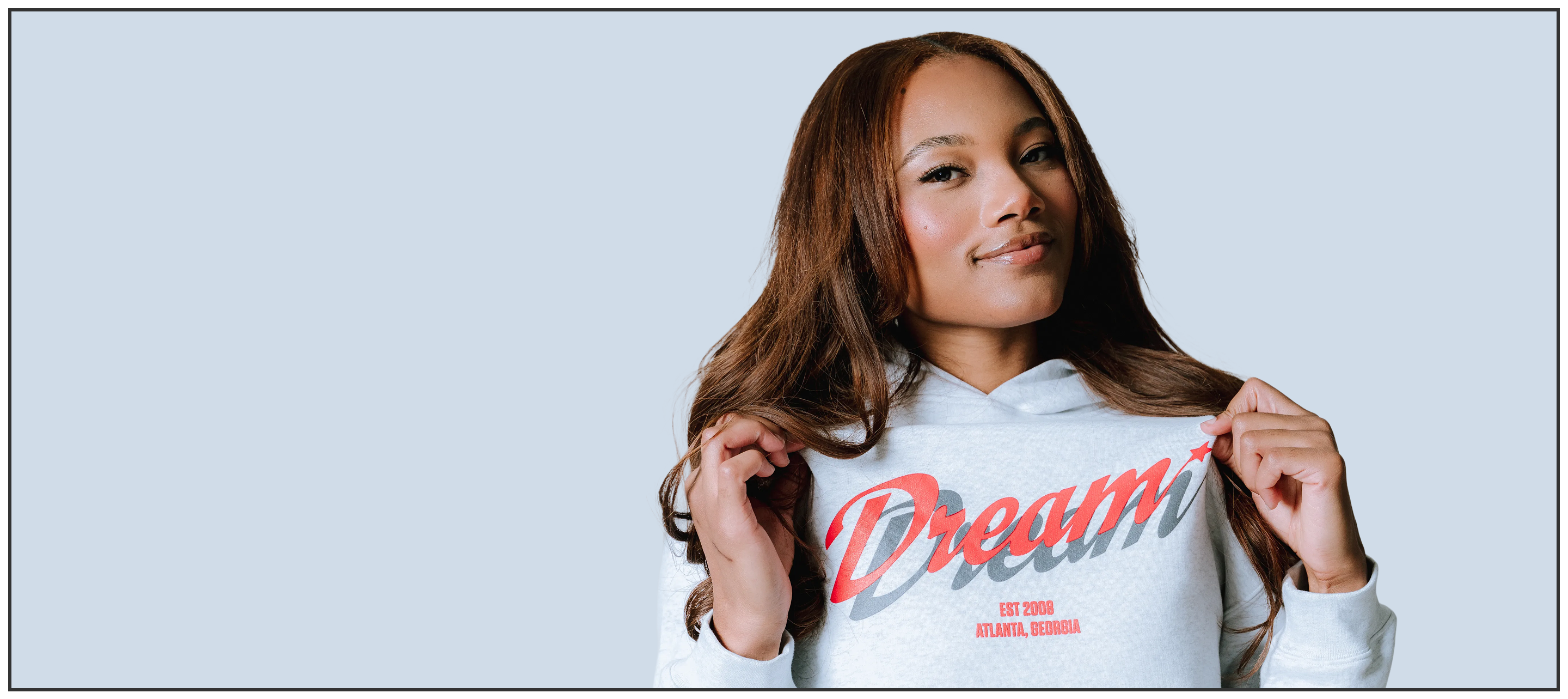 Woman wearing a white hoodie with 'Dream' printed on it against a light blue background