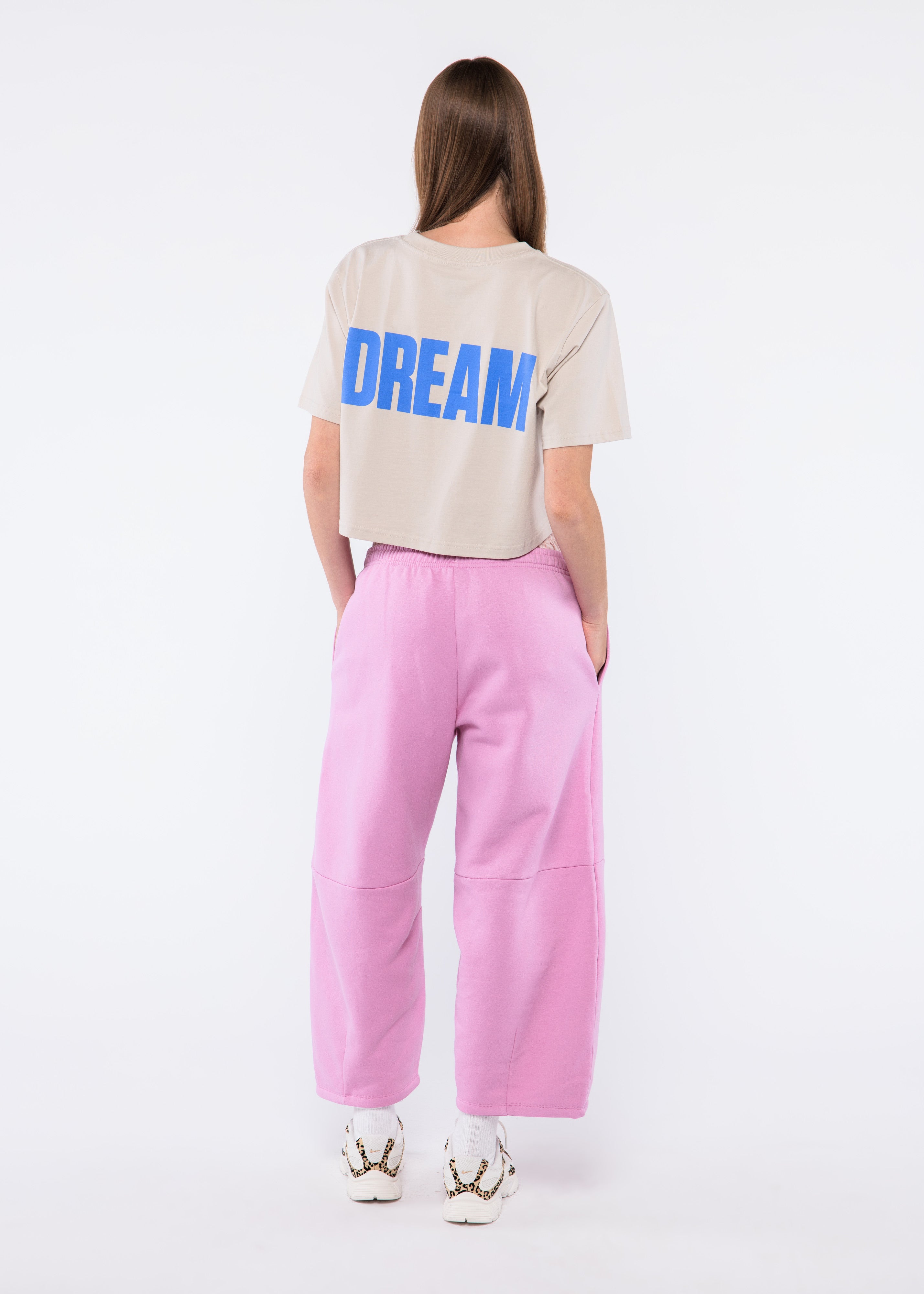 Person wearing a beige t-shirt with 'DREAM' printed on it and pink pants