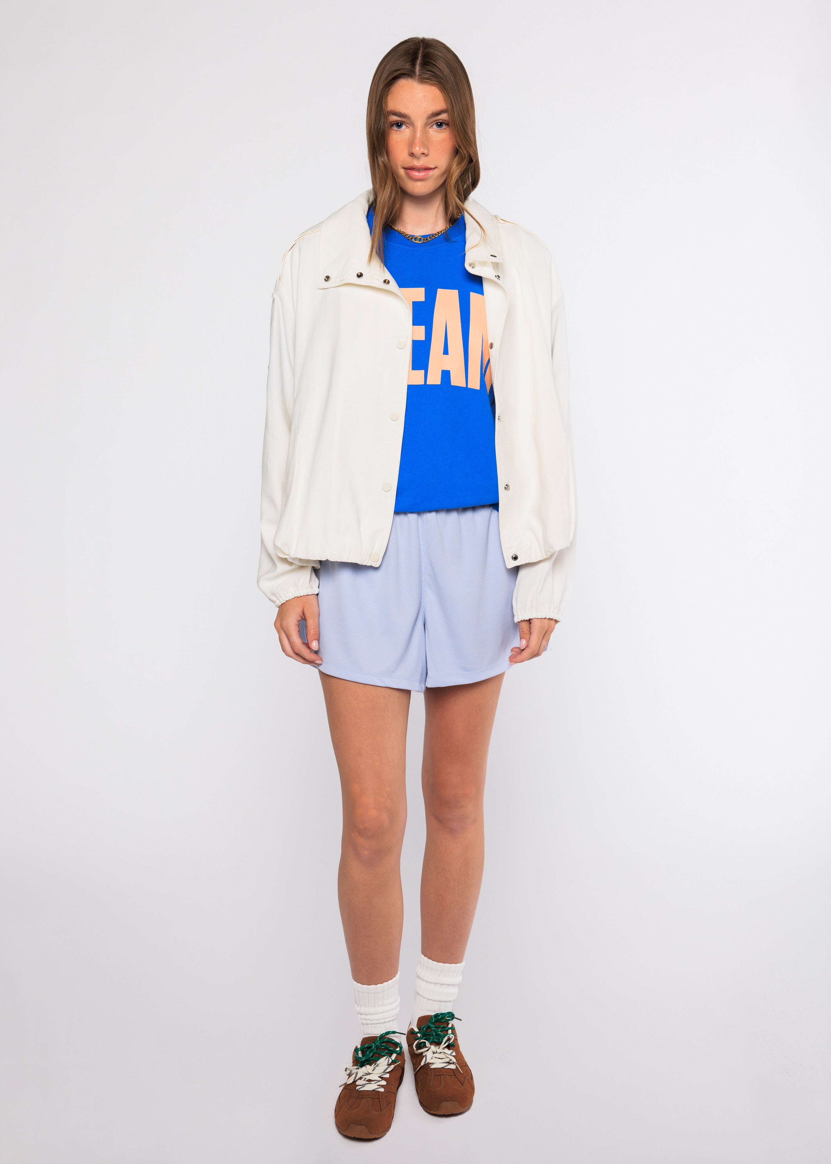 Person wearing a blue graphic t-shirt, light gray shorts, white jacket, and brown shoes