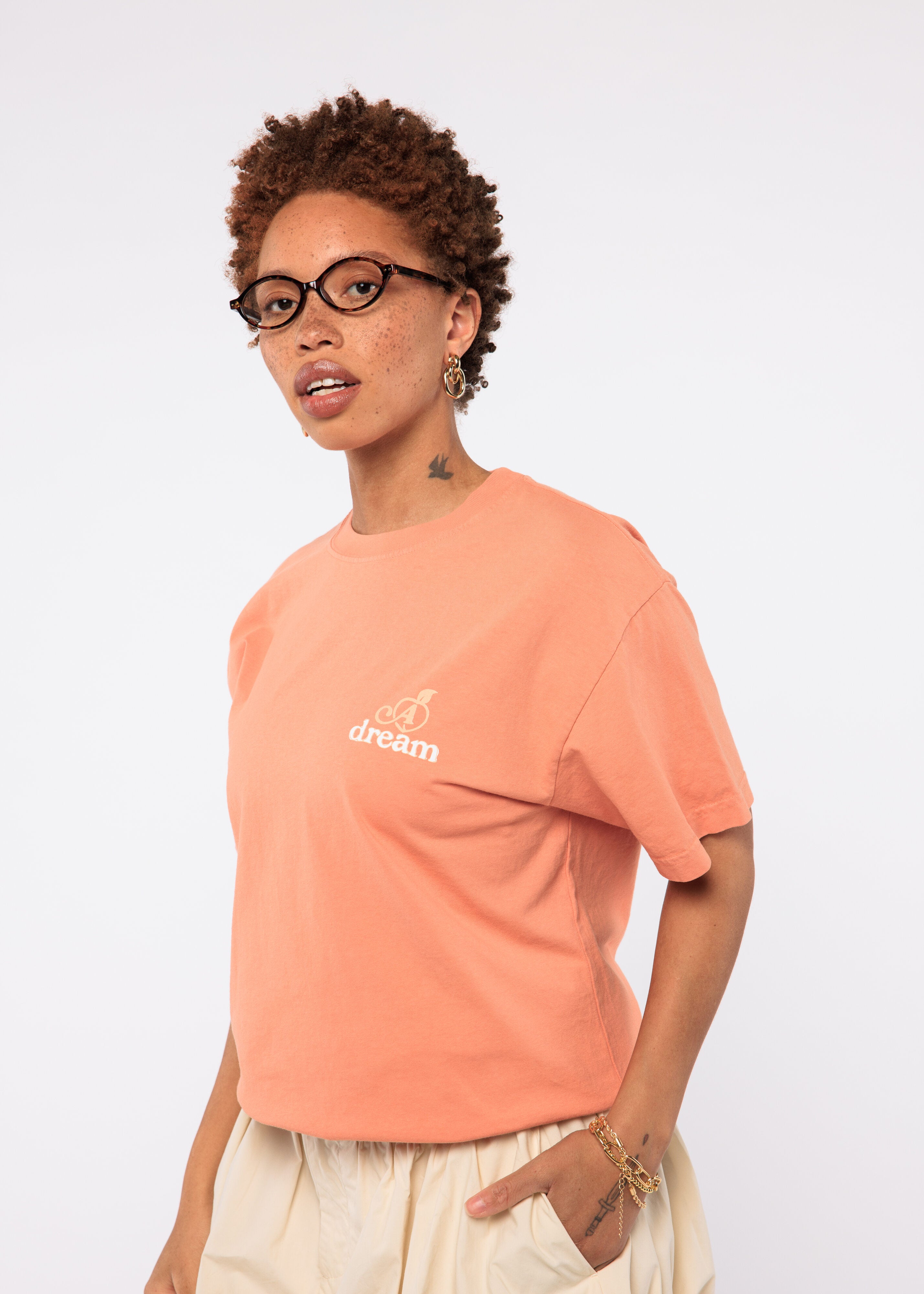 Person wearing a peach-colored t-shirt with a logo and text
