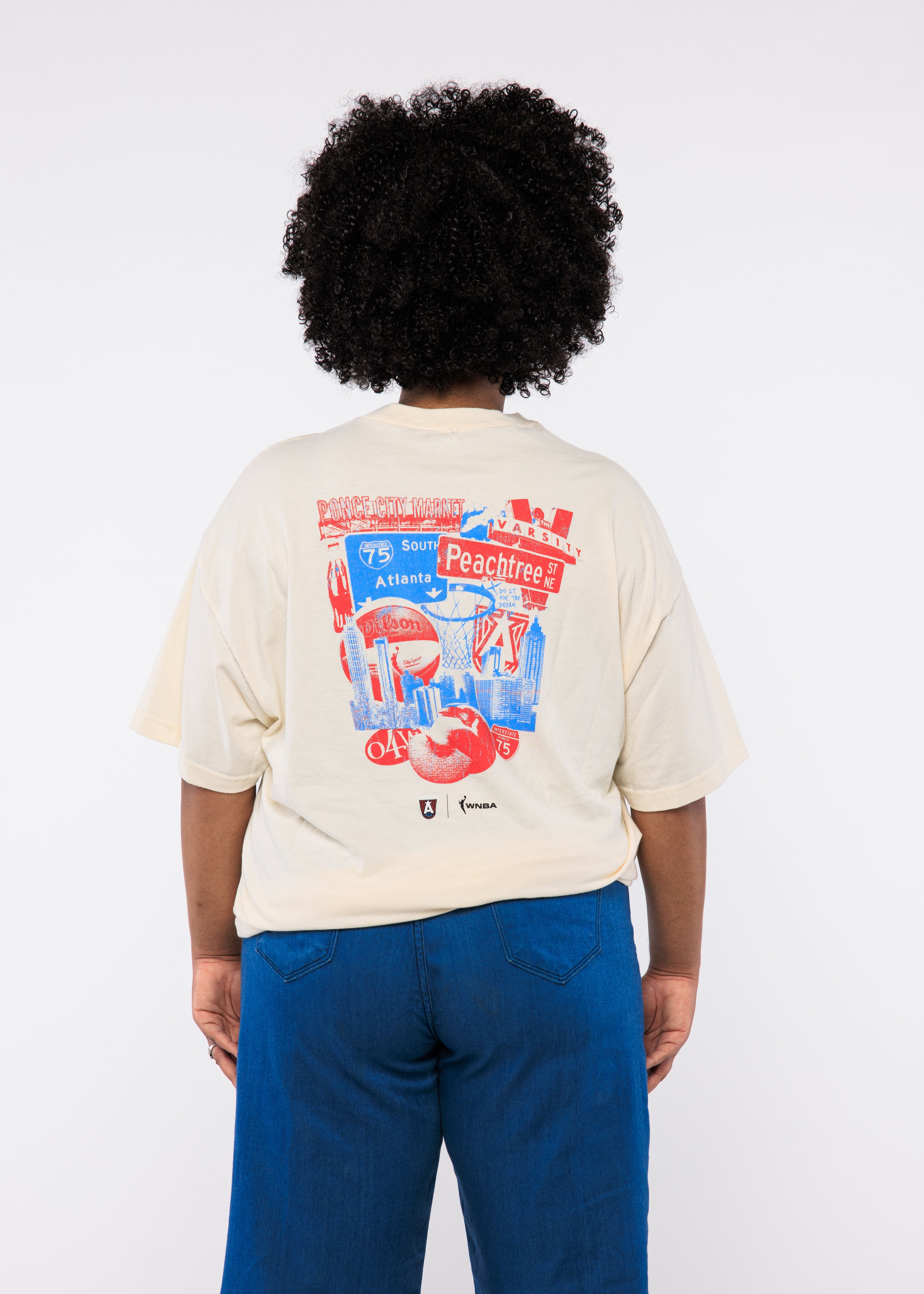 Person wearing a cream t-shirt with colorful graphics on the back