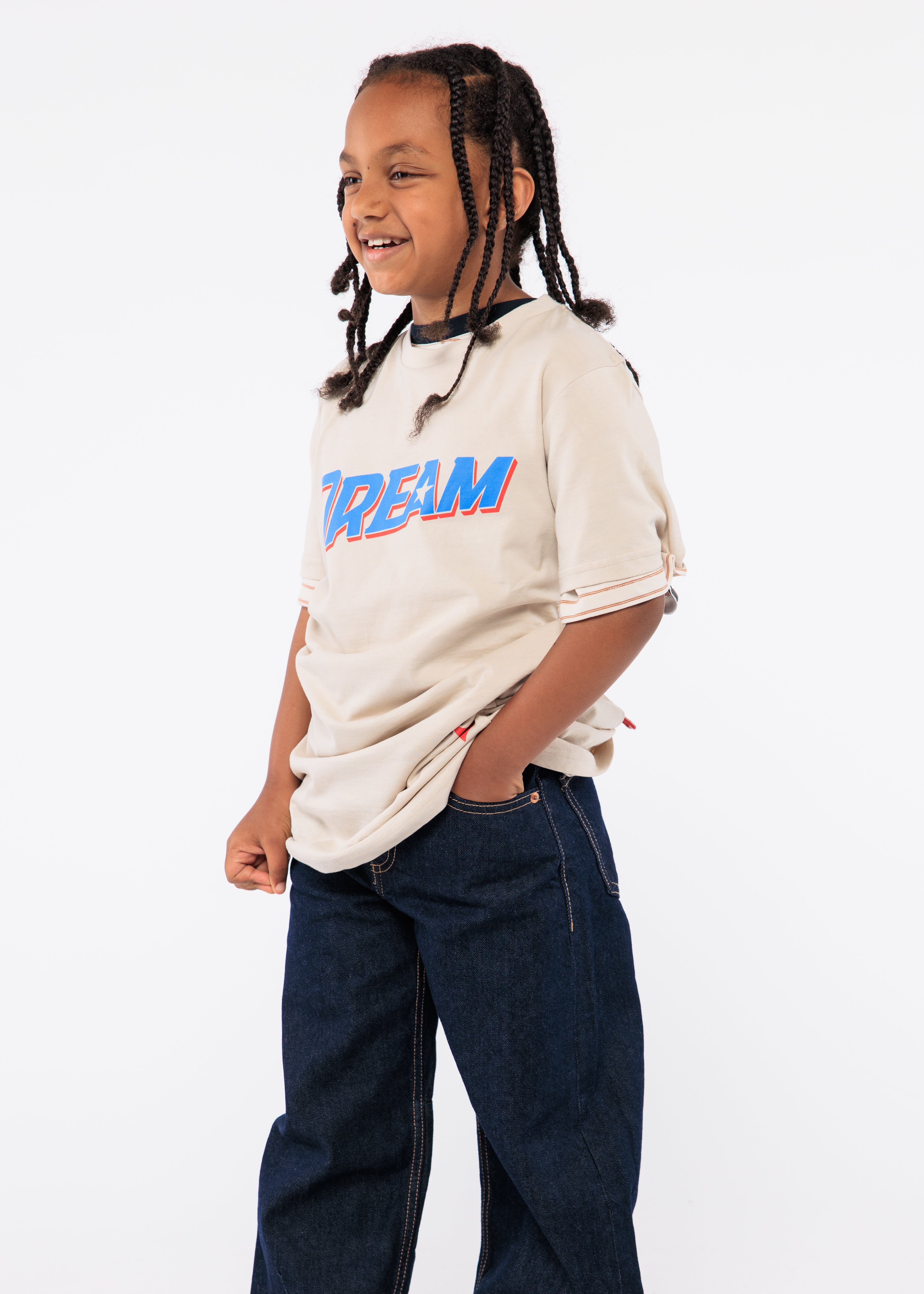 Child wearing a beige oversized shirt with colorful text and dark blue jeans