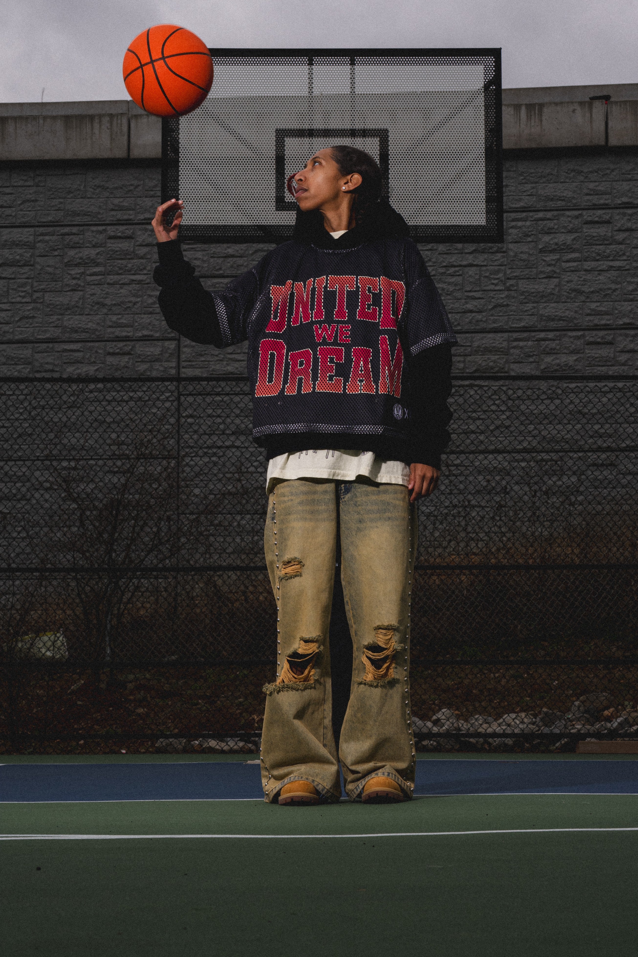 Person holding a basketball on a court with a 'United We Dream' sweatshirt.