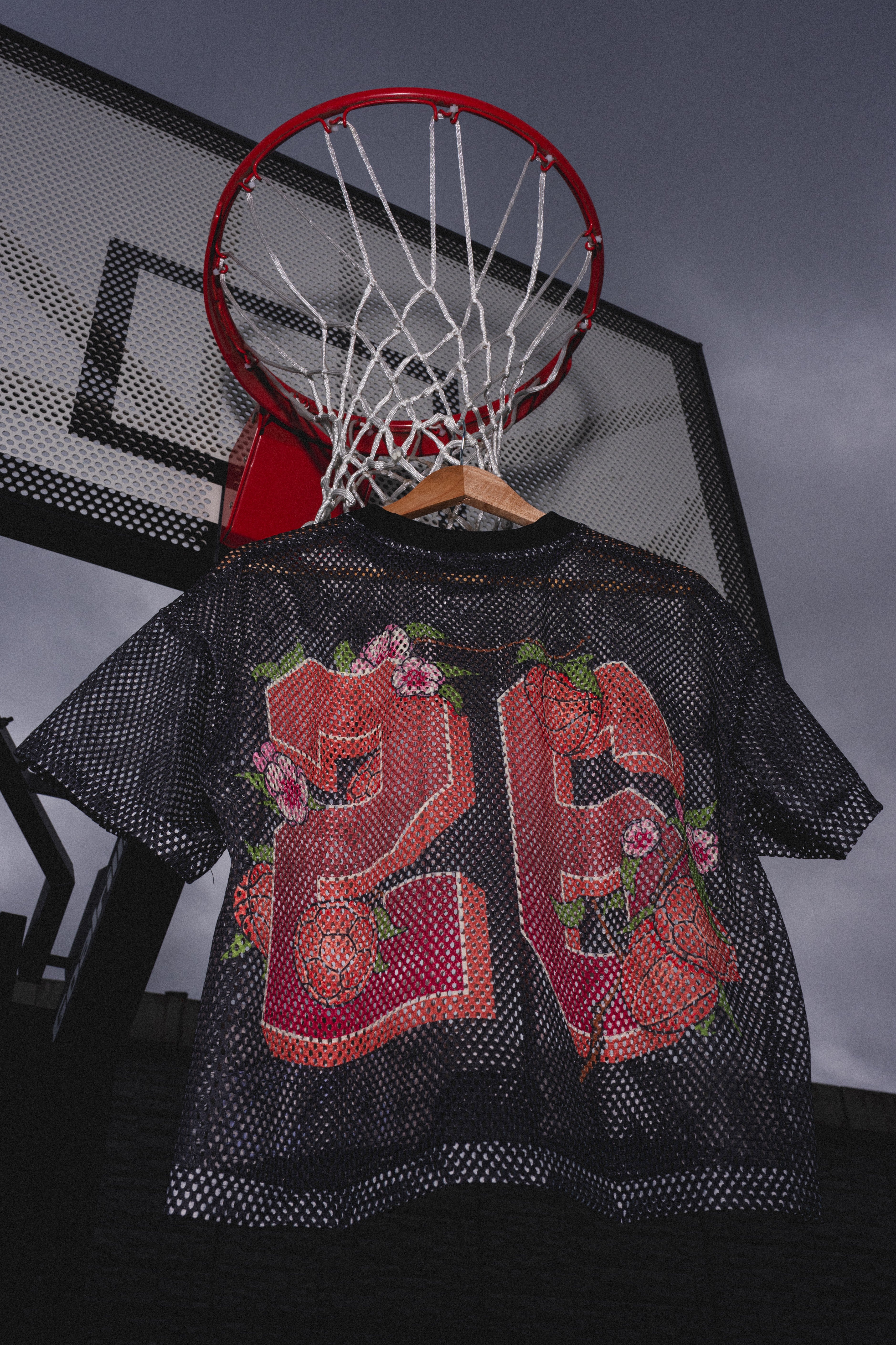 Black sports jersey with pink floral design and number 25 hanging on a basketball hoop.