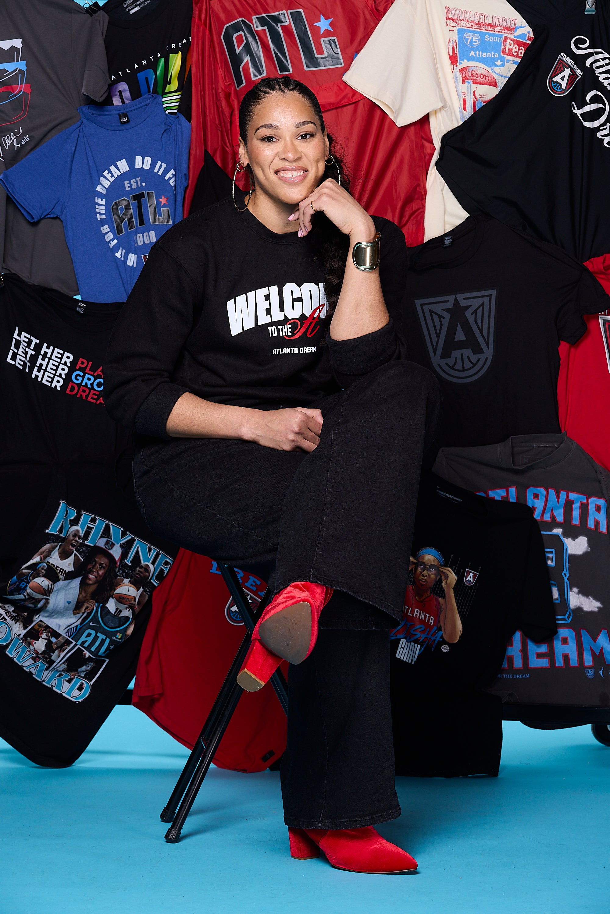 Bri Jones in Welcome to the A Crewneck sitting among various ATL team merch with a colorful background