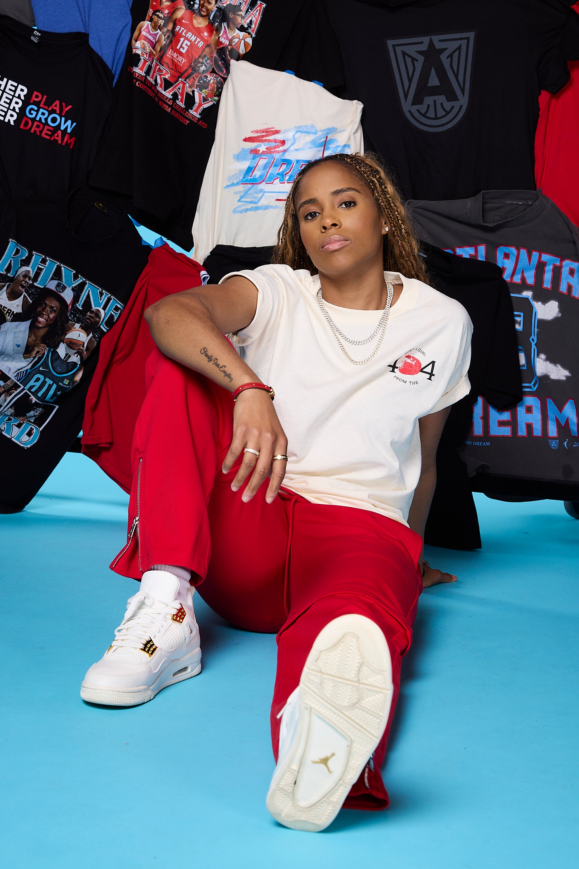 Jordin Canada sitting on a blue floor with colorful t-shirts in the background wearing the Just A Girl from "404" Shirt