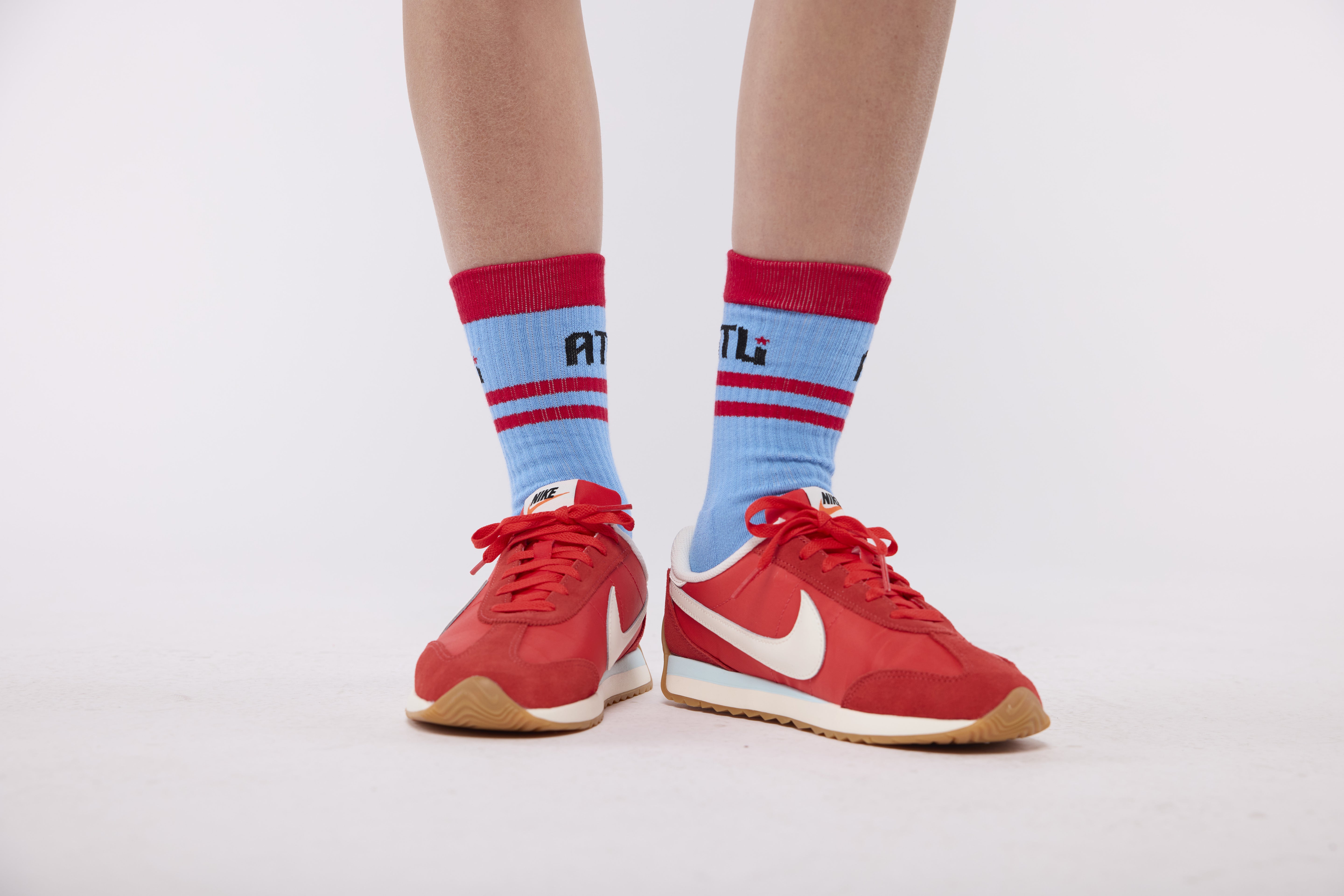 Red sneakers with white Nike logo worn with light blue socks featuring red stripes and a visible brand logo.