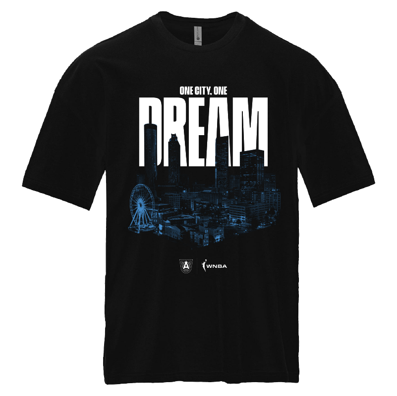 Atlanta Dream Skyline Graphic T-Shirt Black t-shirt featuring the graphic "ONE CITY. ONE DREAM" in bold white lettering across the chest, with a stylized blue silhouette of the Atlanta city skyline, including a ferris wheel. The shirt has a relaxed fit, raised collar, and drop shoulders. Officially licensed WNBA and Atlanta Dream logos are displayed at the bottom.